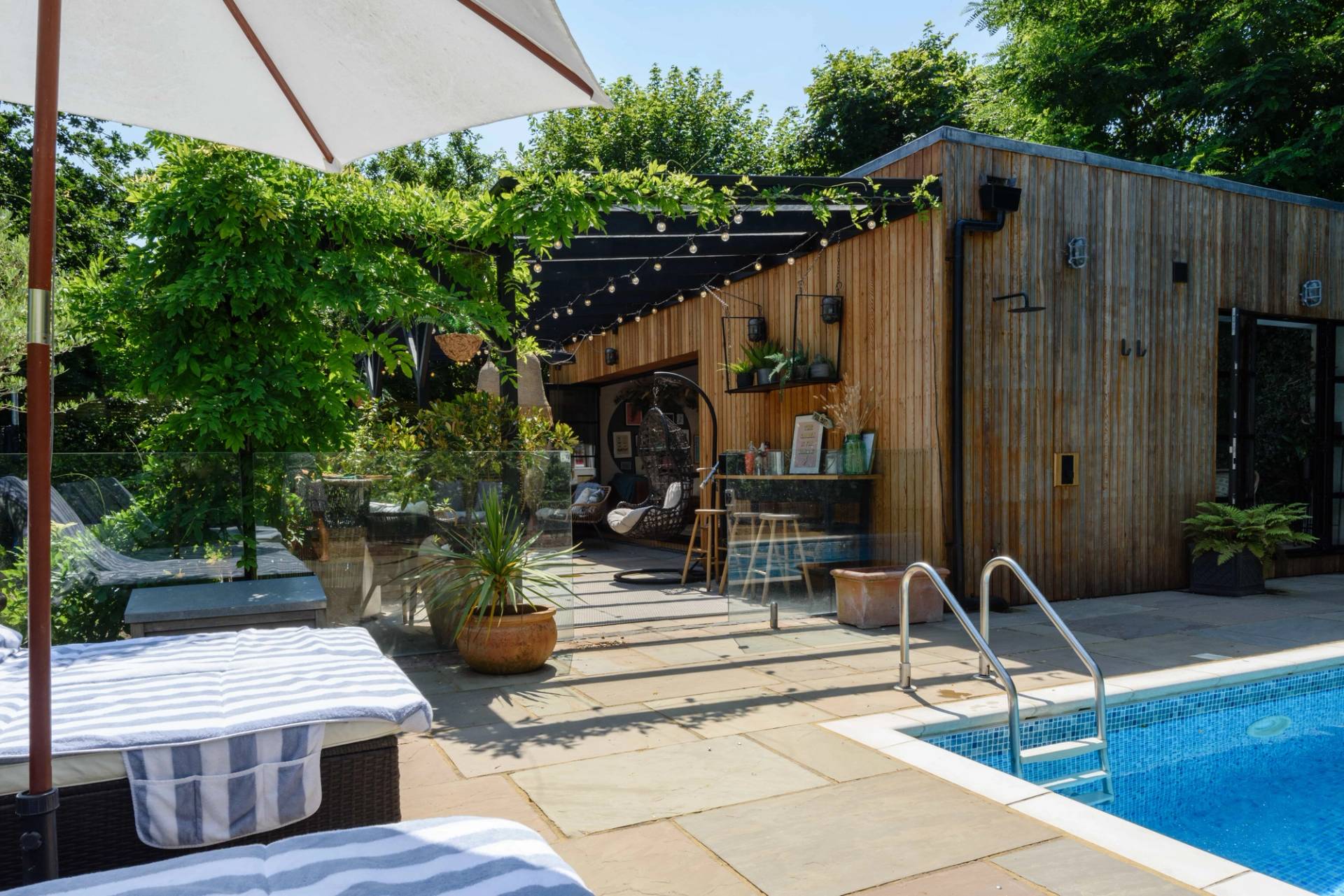 Outdoor swimming pool terrace featuring timber decking, stone paving, and sun loungers, Love Locations TW11.