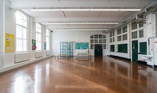 Daylit school hall location space with polished wooden floors and large multi-paned arched windows, listed on Love Locations.