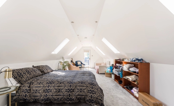 Spacious loft conversion bedroom shoot space featuring sloping eaves and multiple velux roof windows, listed with Love Locations.