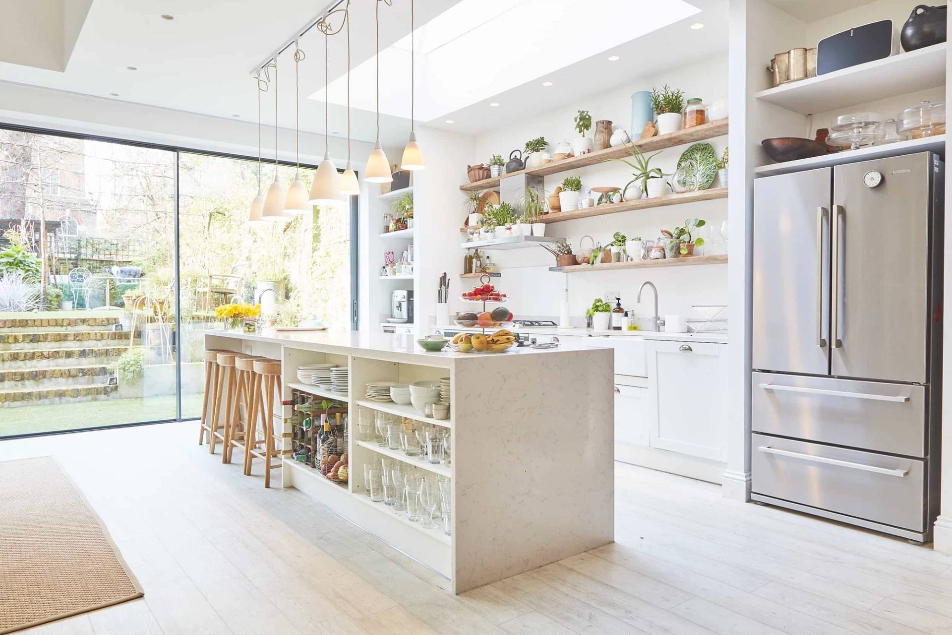 Sunlit kitchen extension in Islington, N5 with a white island counter, open timber display shelving, and glass patio doors, Love Locations N5.