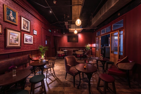 Dimly lit cocktail lounge interior detailing deep red accent walls, low-hanging Edison bulbs, and circular pub tables, ideal for music videos and night-scene filming, Love Locations.