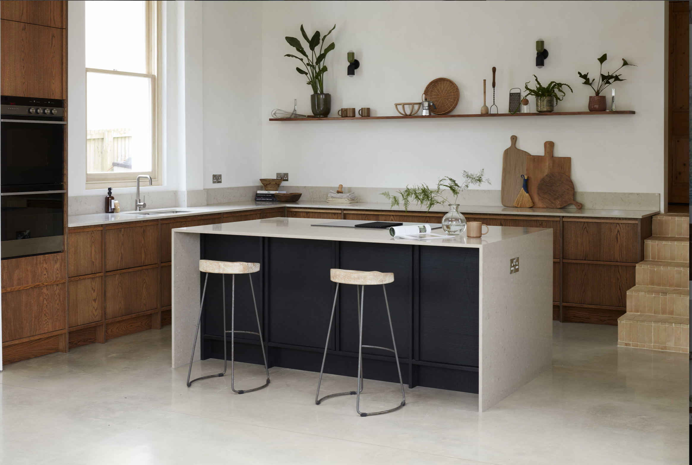 Modern kitchen at Crescent House featuring a large stone island, warm timber cabinetry, polished concrete flooring and minimalist styling.