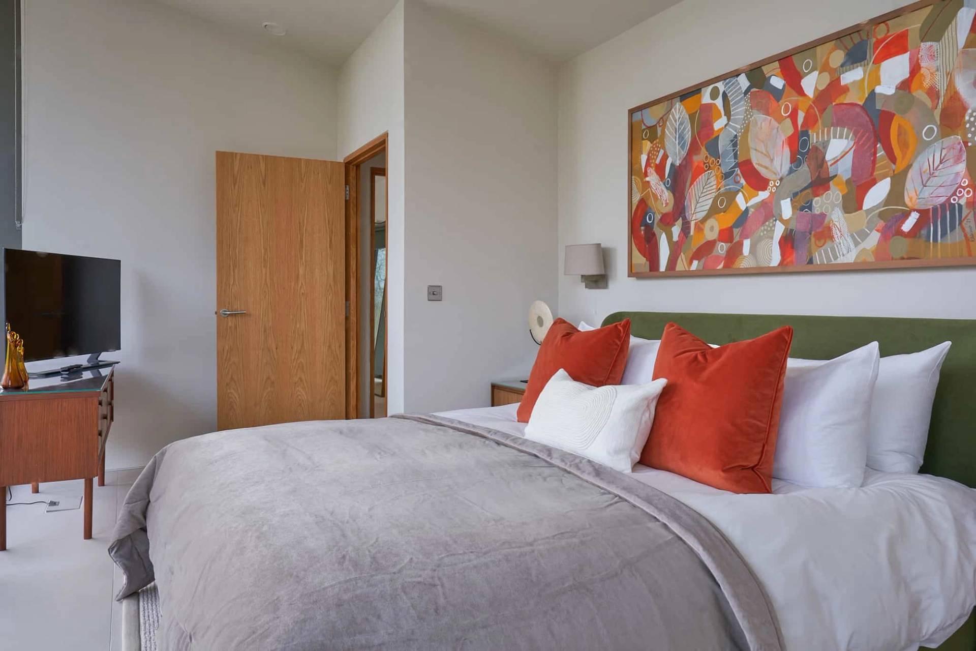 Guest bedroom featuring vibrant red cushions, grey throw, and colorful abstract artwork prints, Love Locations SO21.
