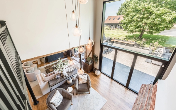 High-angle dramatic perspective of the open-plan barn living area looking out large floor-to-ceiling glass windows, Love Locations.