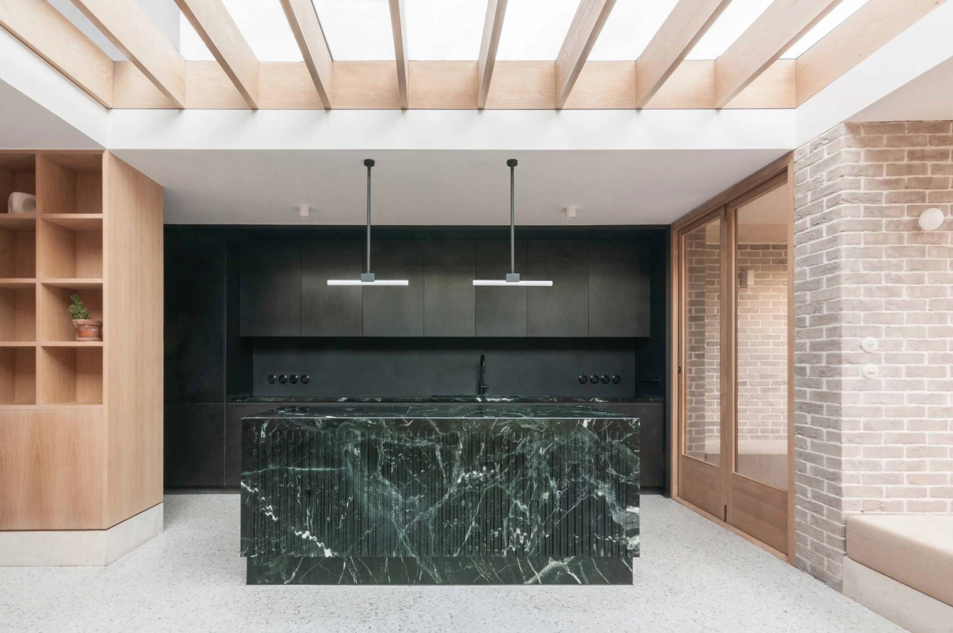 Architectural kitchen shoot space in Hackney N16 via Love Locations, displaying a dark green marble breakfast bar island, black pendant lighting, and exposed ceiling joists.