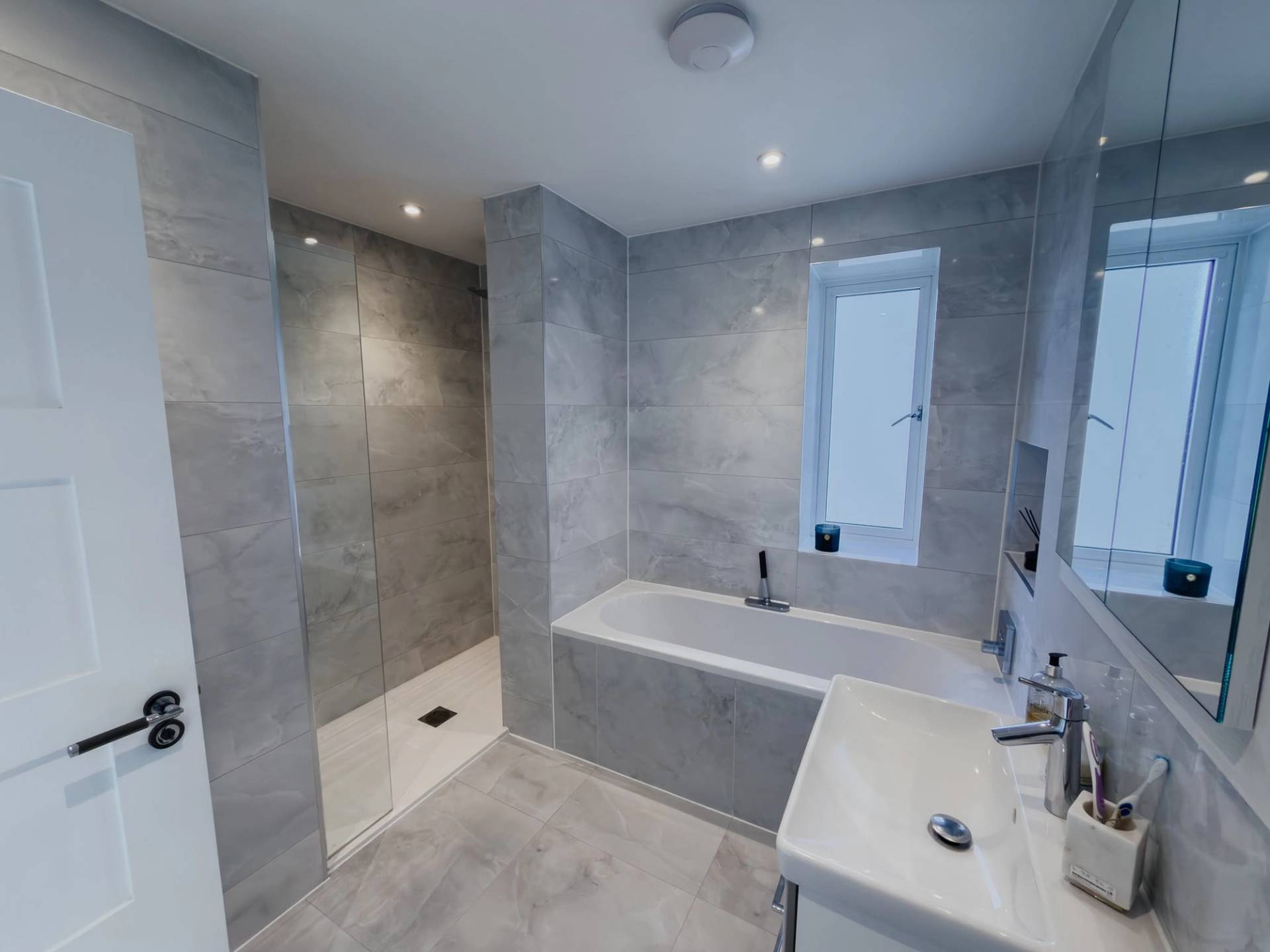Contemporary master ensuite bathroom film location in Barnet EN4 through Love Locations, with grey marble wall tiles, walk-in glass shower, and soaking bathtub.
