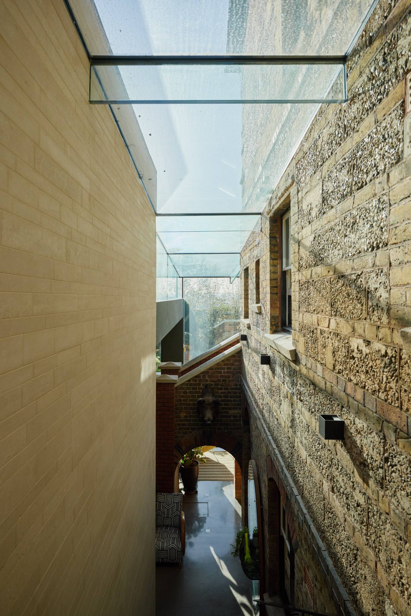 Glazed roof bridge corridor looking down between Victorian brickwork and smooth modern plaster walls, Love Locations SW20.