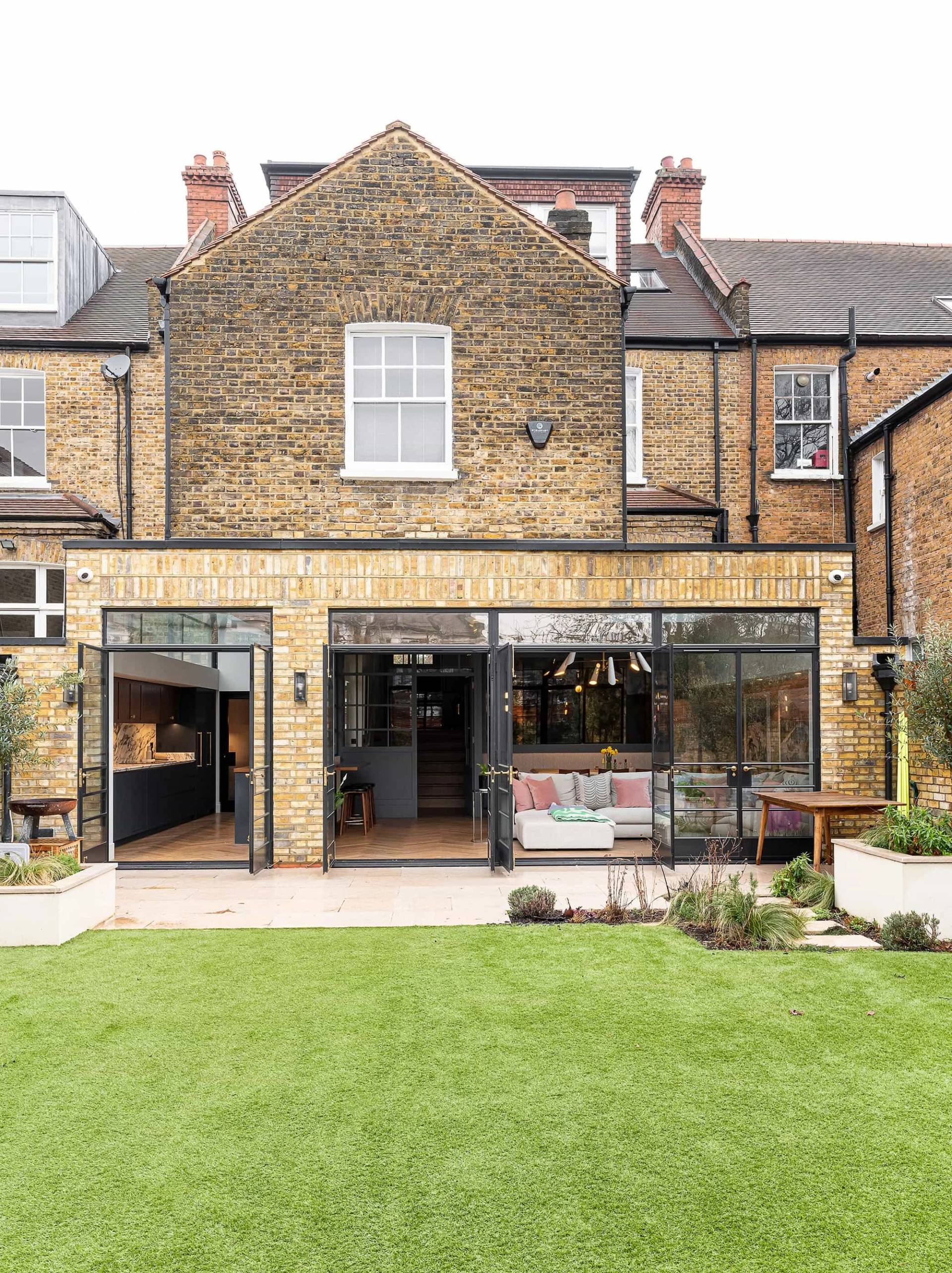 Rear garden elevation of a Victorian property with black crittall patio doors opening onto a raised stone terrace and lawn, ideal for TV drama filming, Love Locations NW6.