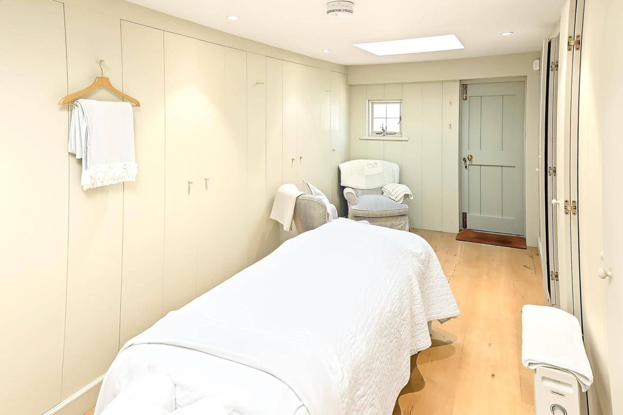 Private massage or wellness treatment room location house in Gloucestershire GL7 from Love Locations, featuring a professional treatment bed, neutral panelled walls, and soft lighting.
