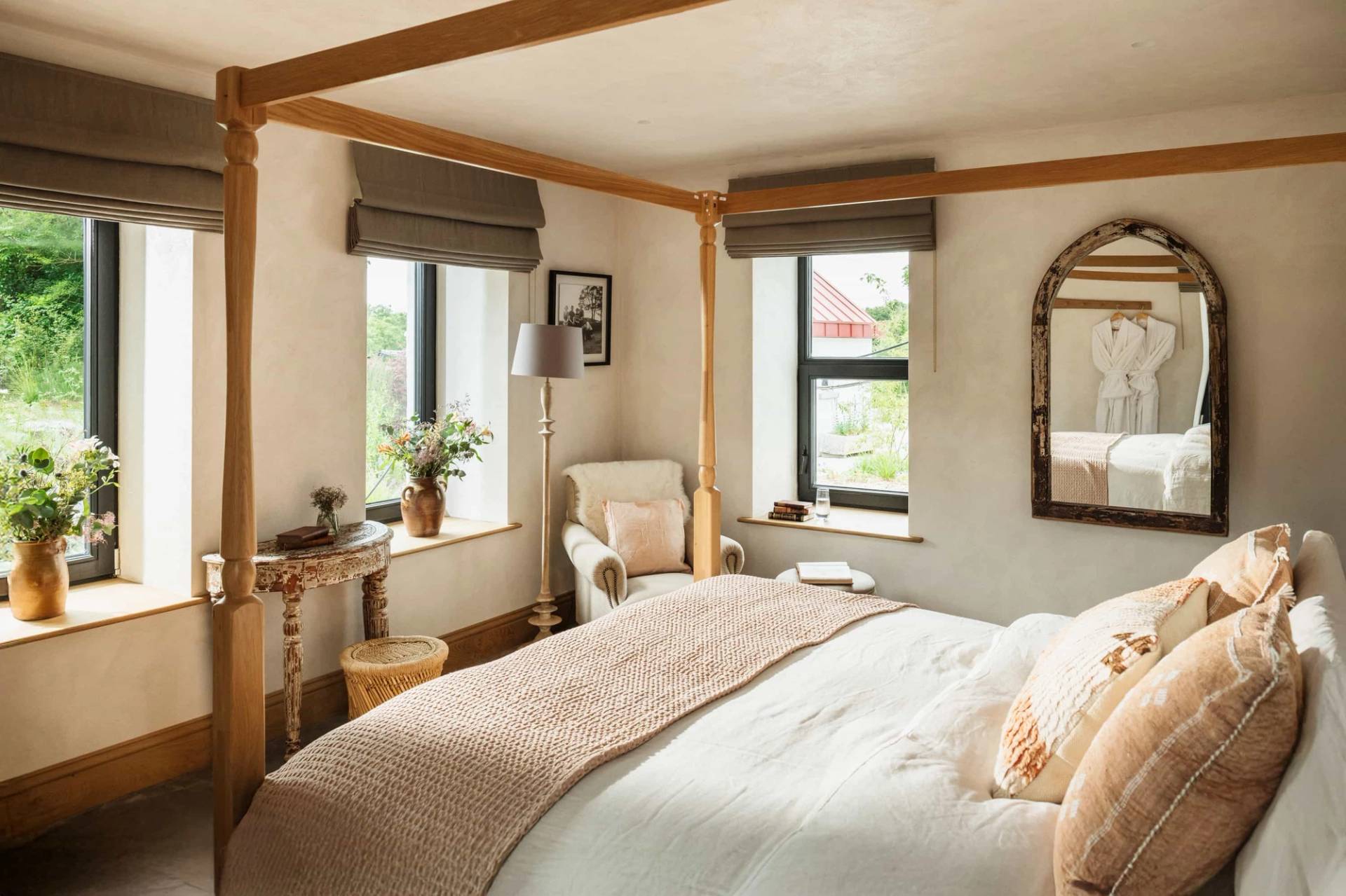 Light neutral bedroom shoot location in Castleblayney County Monaghan Ireland via Love Locations, displaying a wooden bed, cozy armchair, and picture windows looking over green fields.