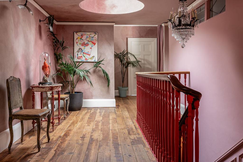 Broad view of a spacious first-floor landing with exposed wooden floorboards and a red balustrade, a prime fashion shoot location by Love Locations.