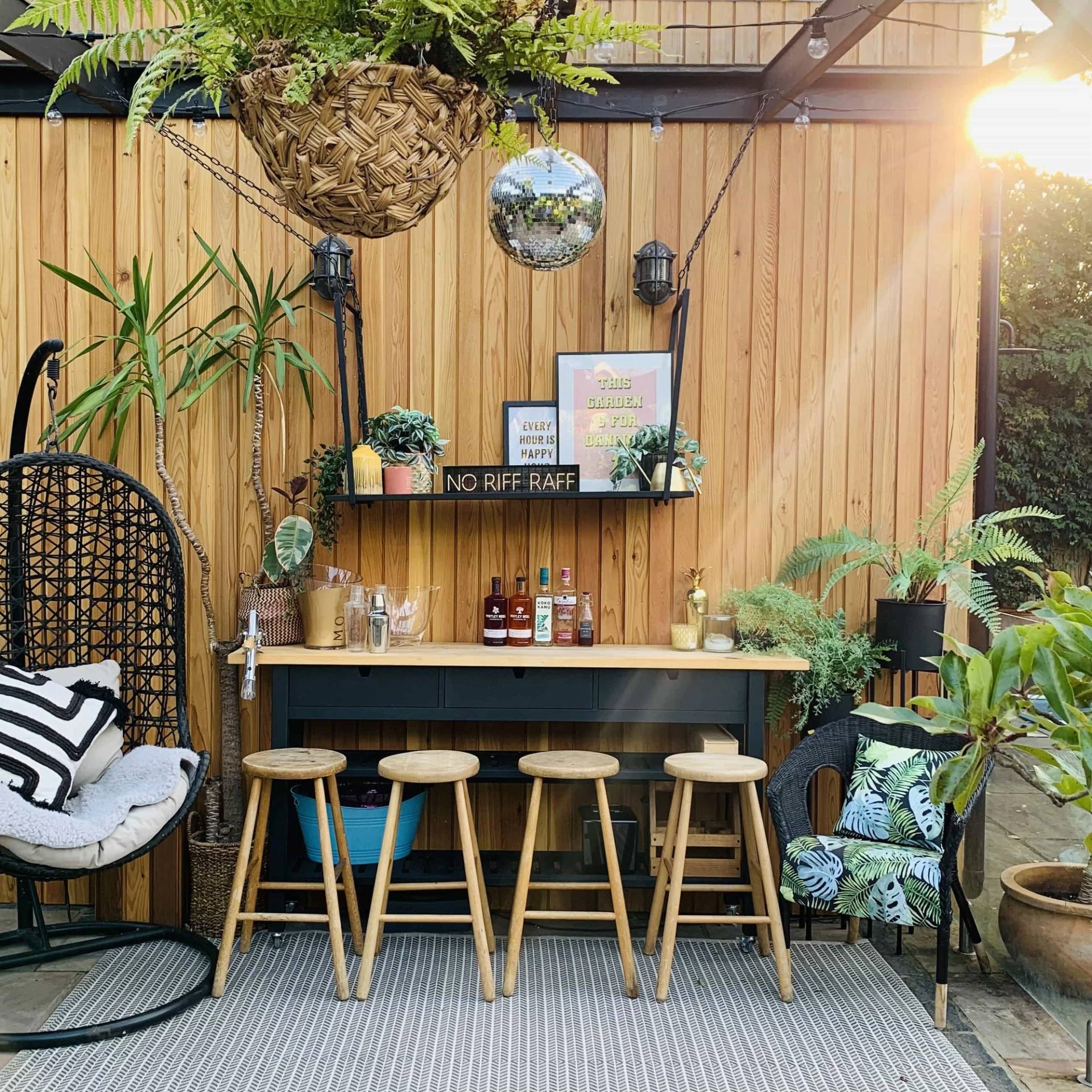 Outdoor garden bar setup under a wooden pergola with woven bar stools and hanging planters, Love Locations TW11.