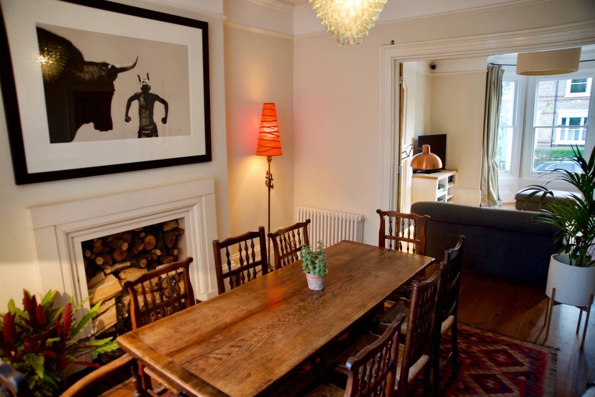 Traditional dining space featuring a period fireplace, wooden table, and red lamp shade accent, Love Locations TW1.