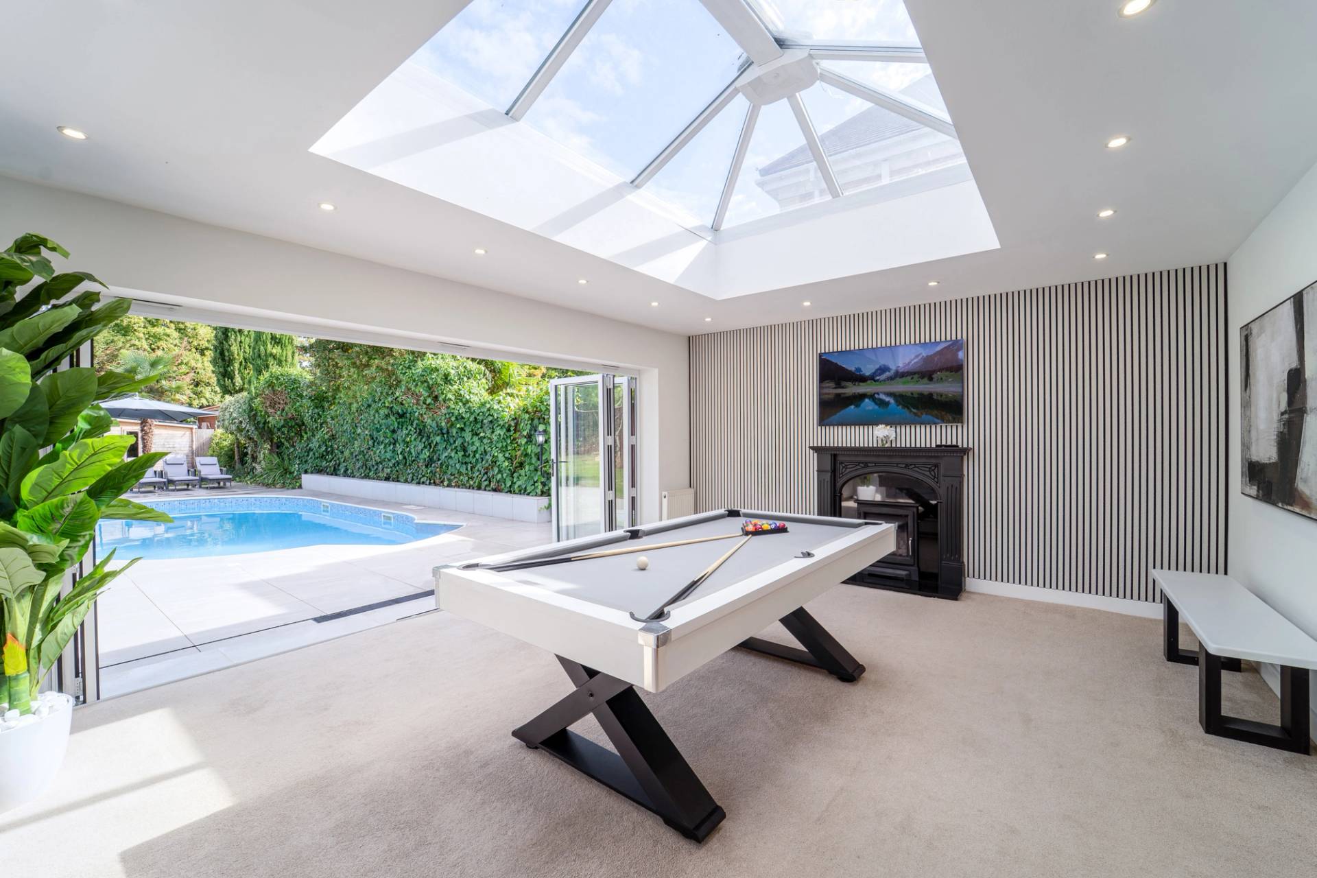 Bright entertainment space with a pool table, wall-mounted TV, and glass lantern roof skylight, Love Locations RM11.