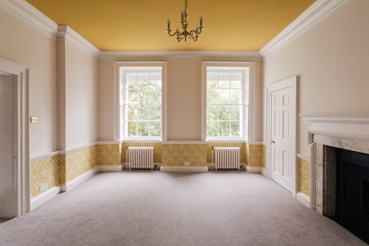 Spacious period room with ochre yellow wallpaper and ceiling accent trim, twin sash windows, and beige carpet, ideal for fashion editorial shoots, Love Locations SE15.