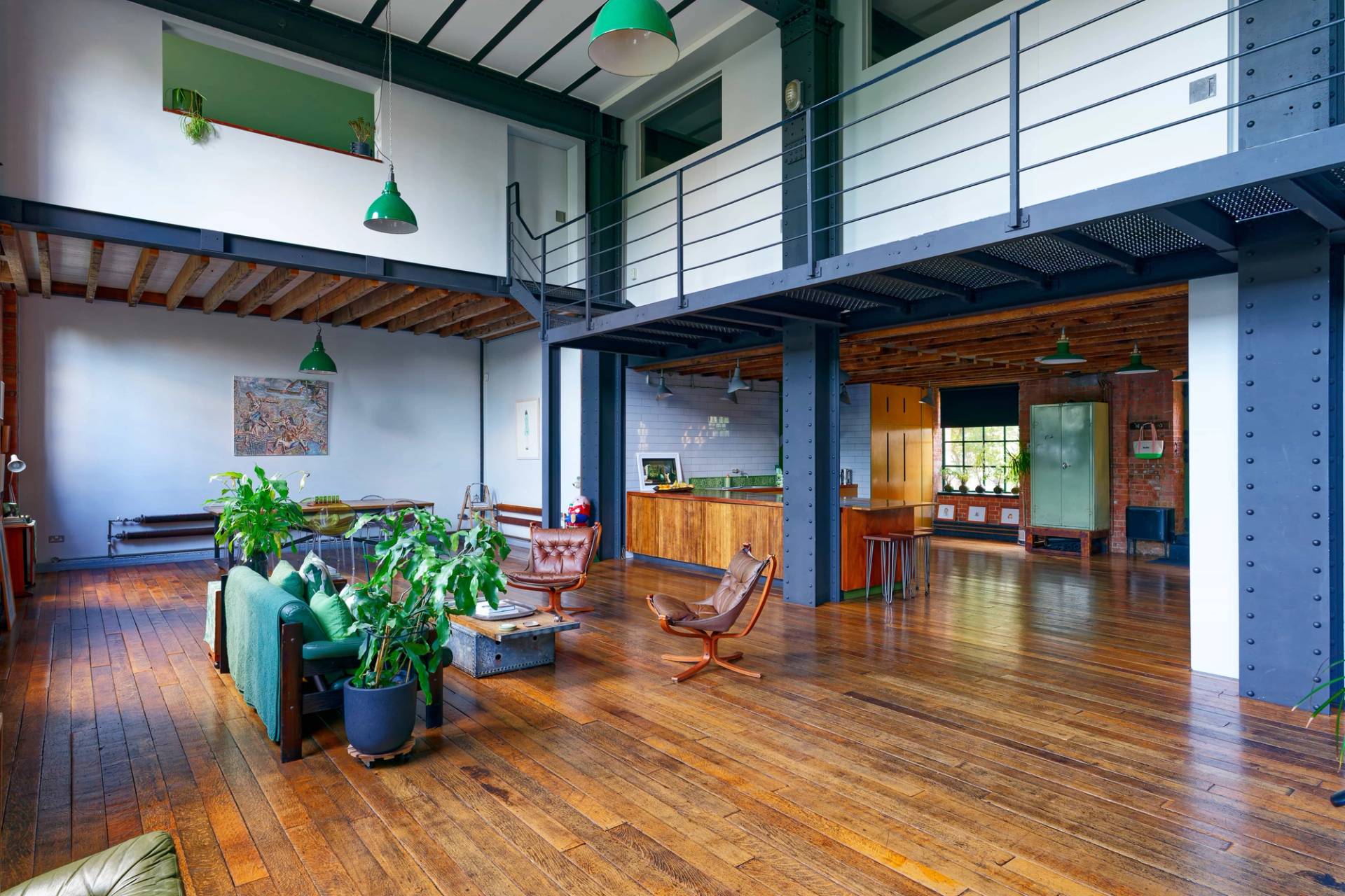 Wide-angle perspective of an industrial warehouse conversion showcasing steel mezzanine balconies, brick arches, and green pendant lights, Love Locations E14.