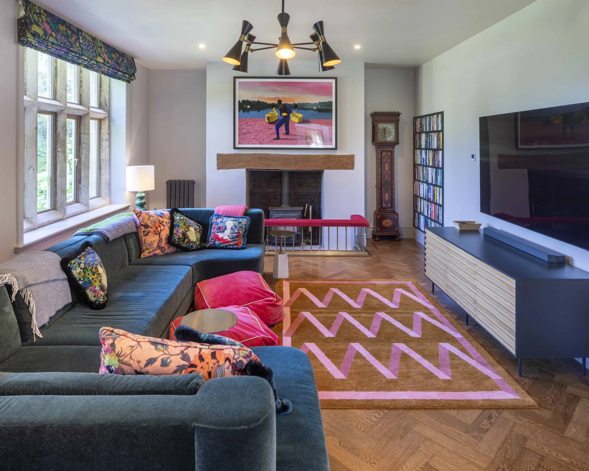 Bright family room with a green corner sofa, colorful floor rug, wall-mounted television, and fireplace, Love Locations OX7.