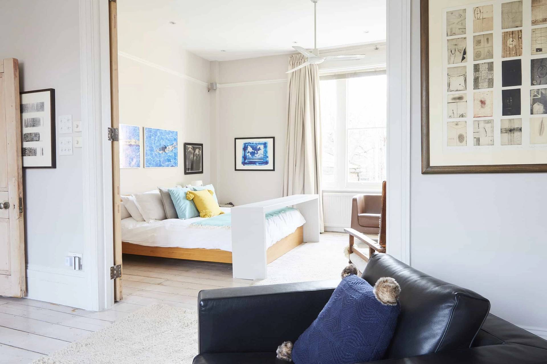 Light-filled master bedroom featuring a low-profile timber bed, dark leather armchair, and sash window views, Love Locations N5.