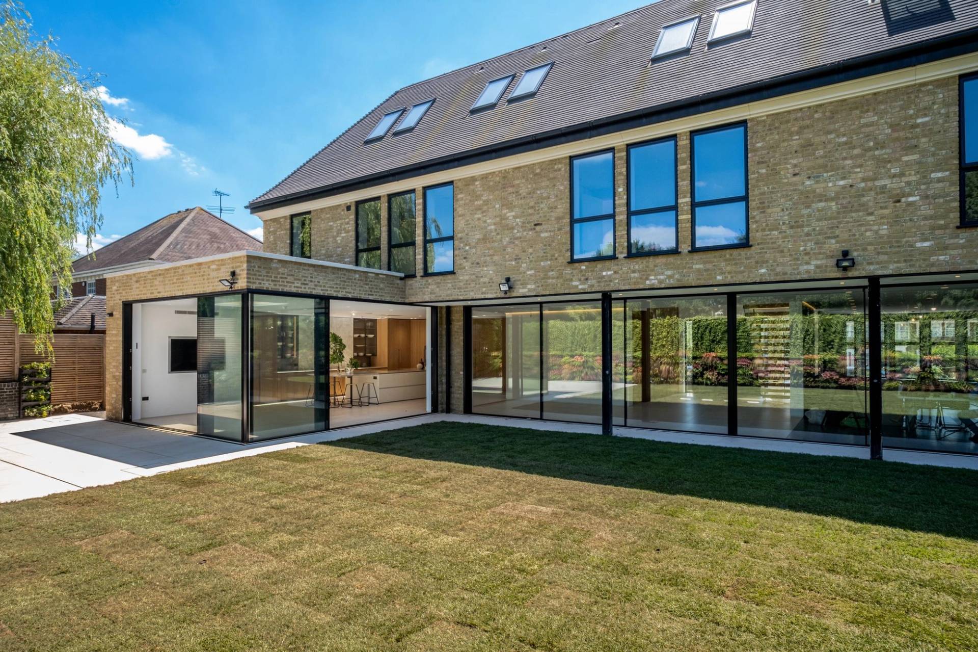 Rear exterior view of a modern yellow-brick house showing expansive glass sliding doors and top-floor dormer windows, ideal for establishing film shots, Love Locations N3.