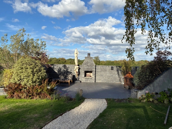 Sunlit stone terrace and outdoor entertaining patio in Essex CM4 from Love Locations, showing built-in stone walls, a fireplace feature, and open countryside vistas.