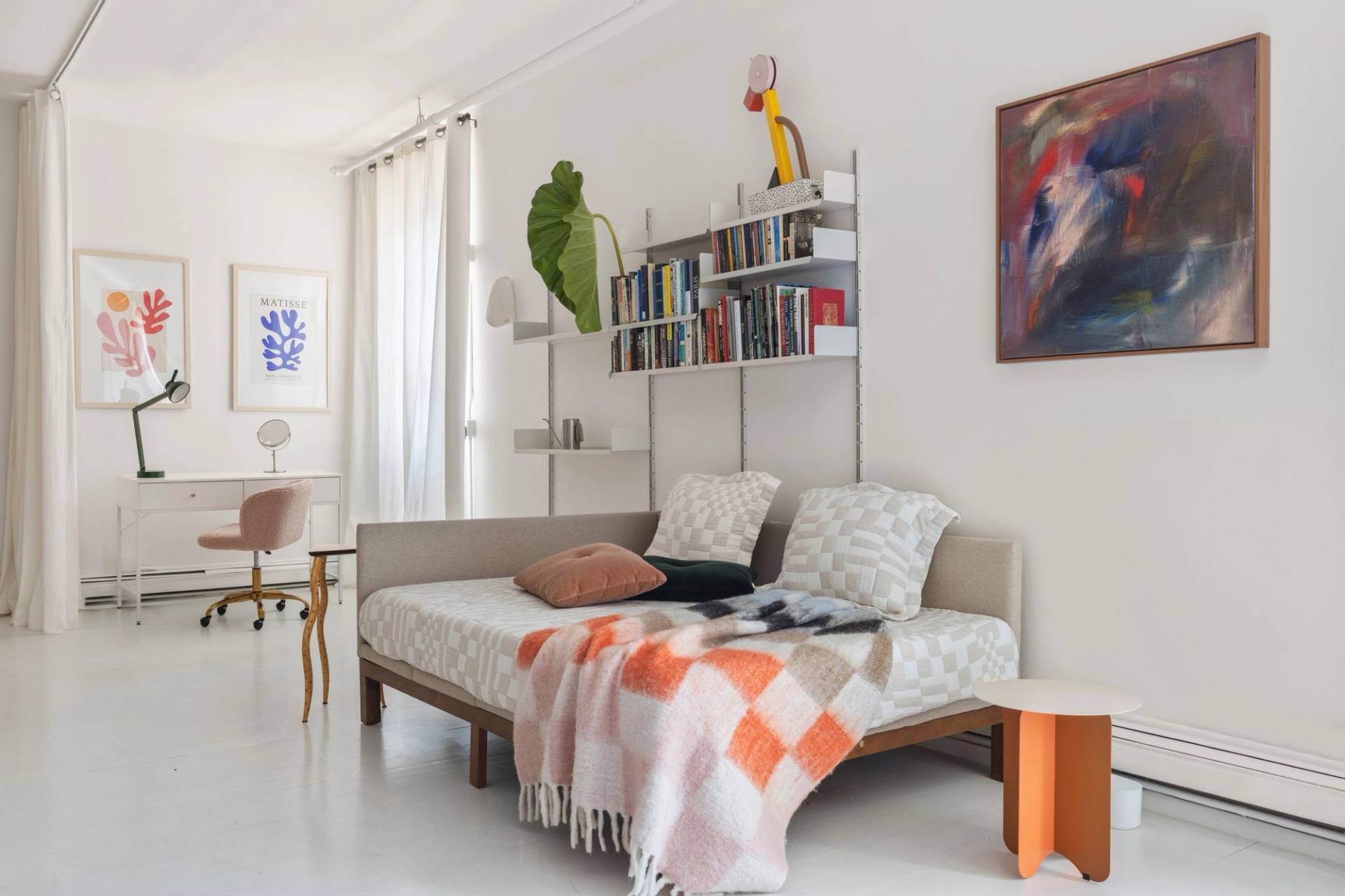 Sunlit bedroom shoot venue in an all-white Tribeca NYC loft through Love Locations, featuring light wood bed frame, orange patterned textiles, and wall shelves.