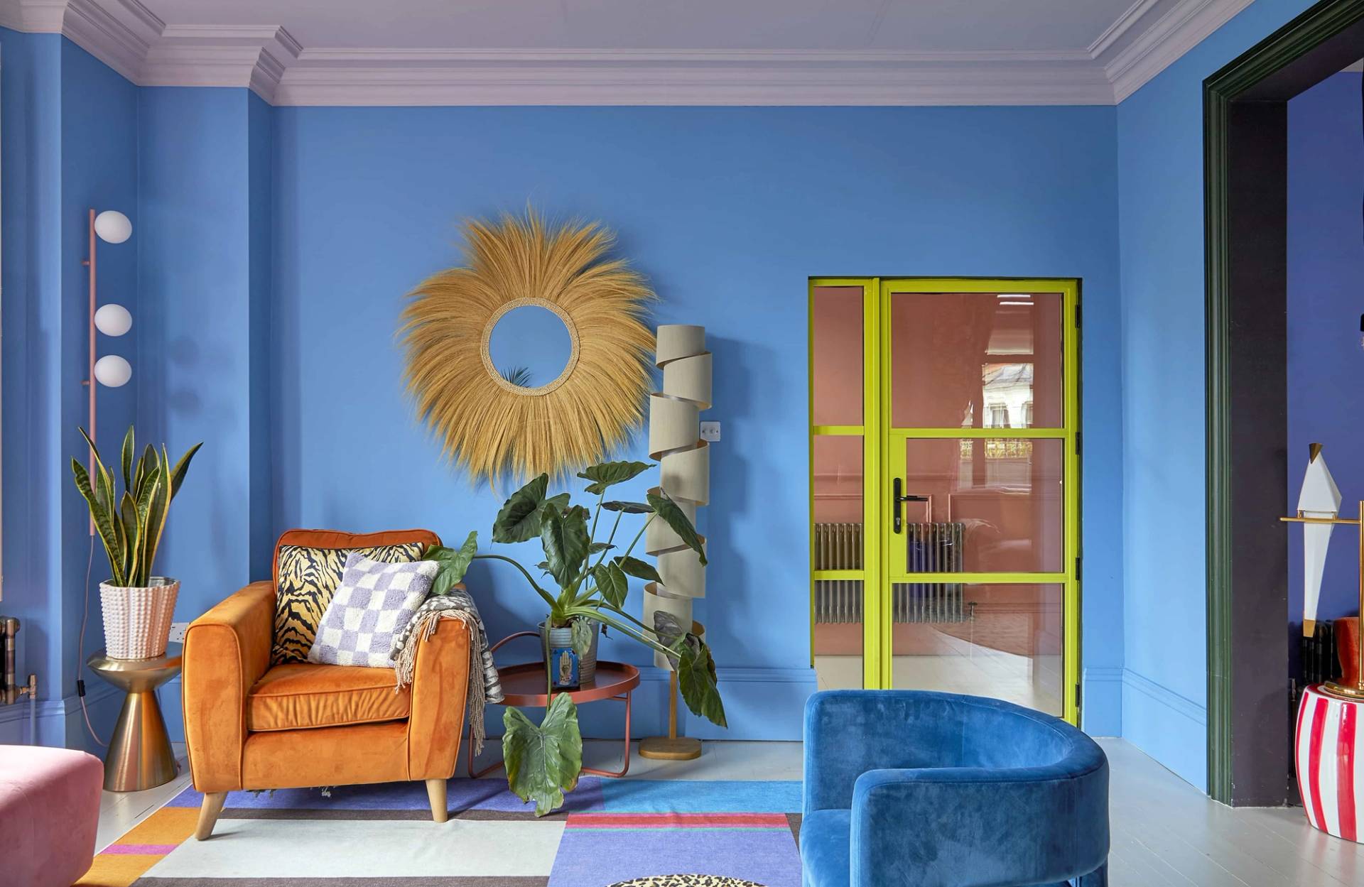 Bright blue reading nook with a sunburst mirror, tan armchair, and yellow framed doorway, Love Locations Catford.