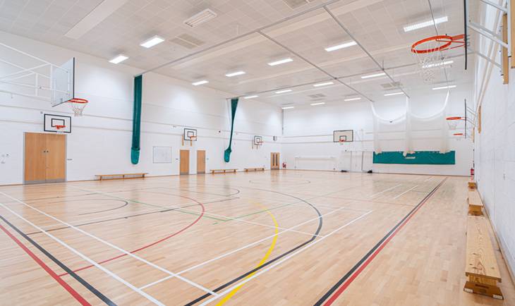 Full-size indoor school sports hall photo location with timber floors, green wall padding, and court nets through Love Locations.