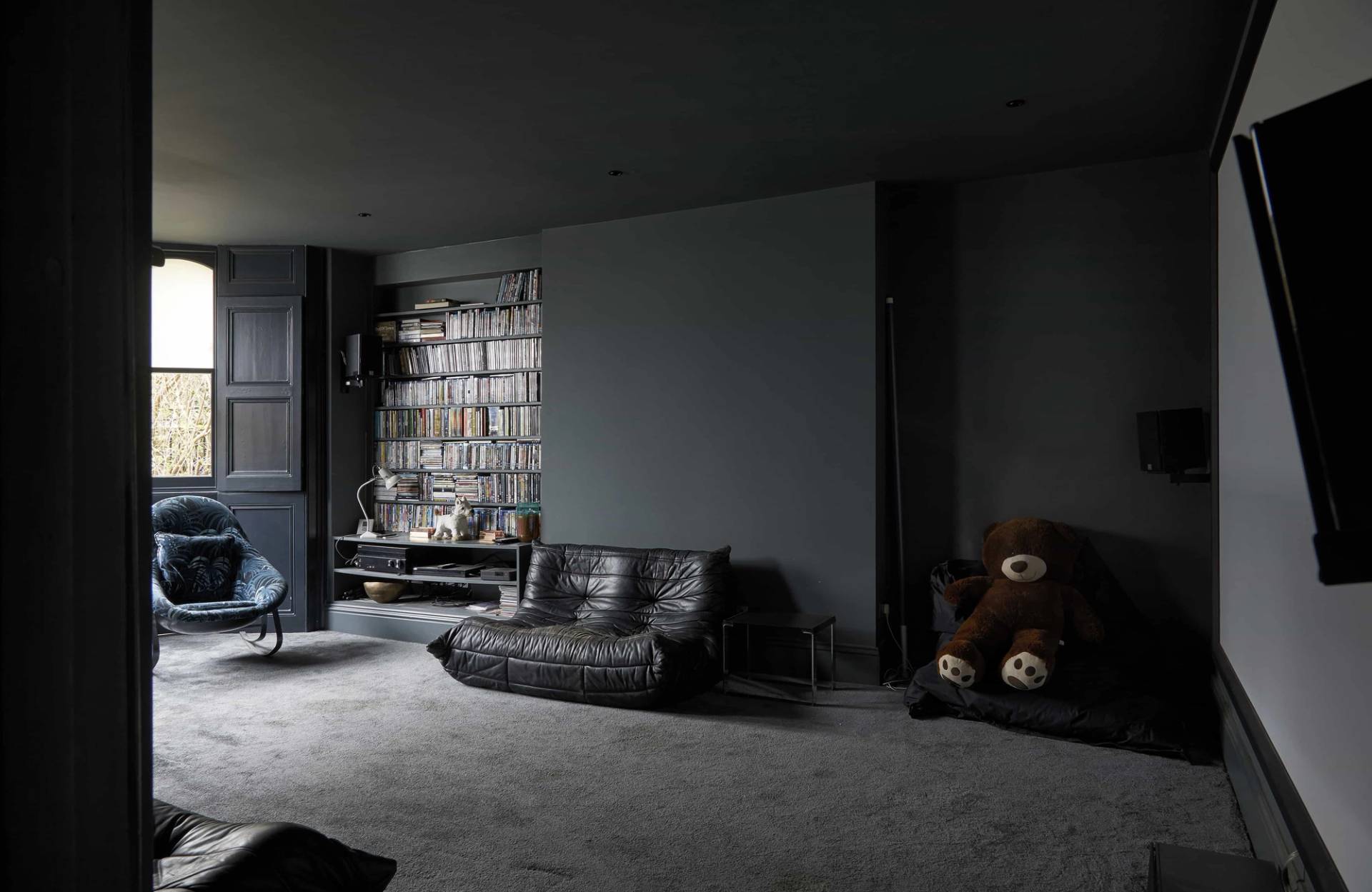 Atmospheric dark lounge with black leather sectional sofa, dark grey walls, and low ambient lighting, Love Locations N16.