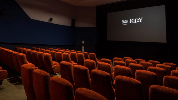Close-up side profile of the tiered red velvet cinema seats and deep blue accent walls inside The Ritzy Screen 3 filming location via Love Locations.