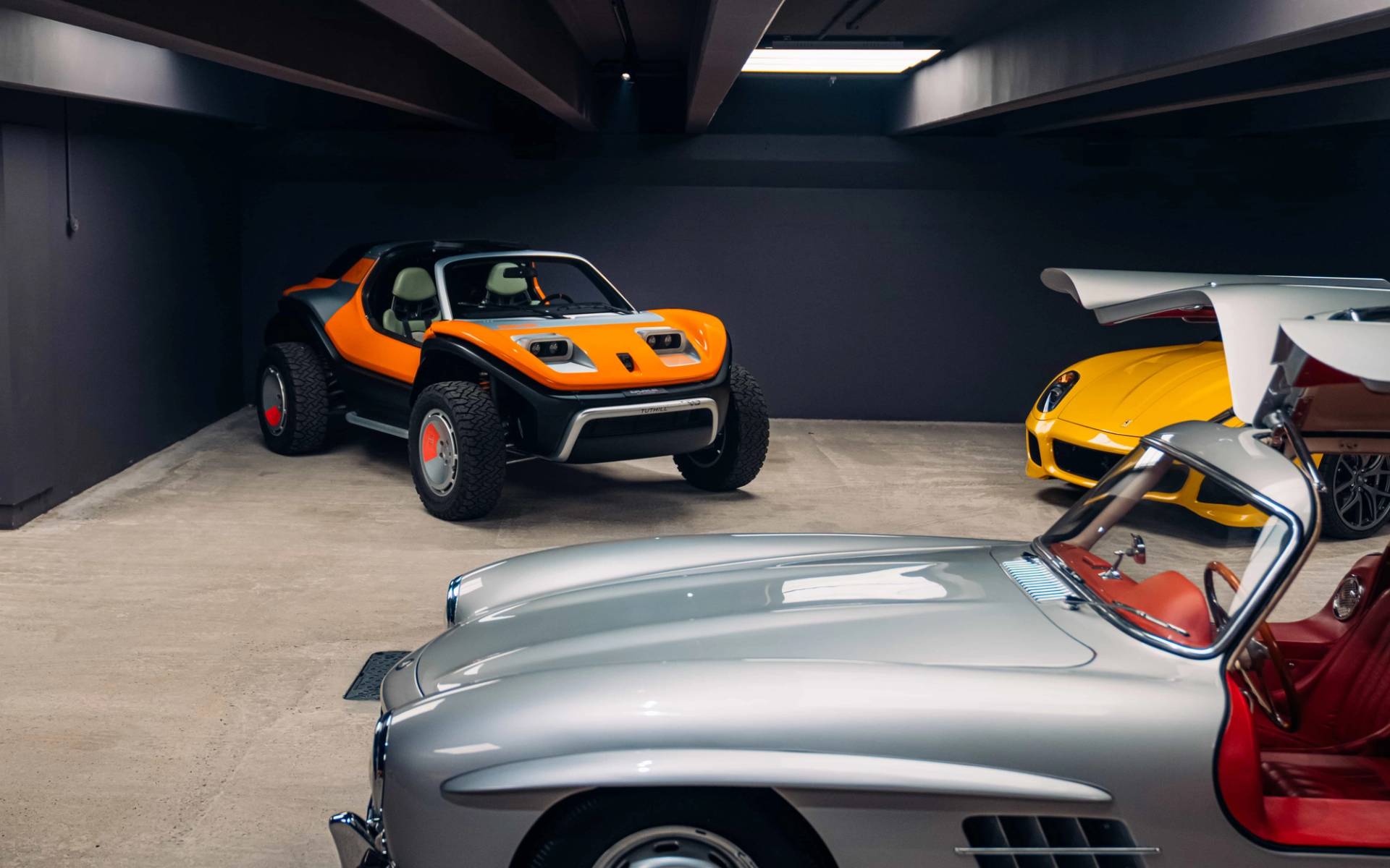Collection of rare supercars including a silver classic and orange buggy parked inside a subterranean vault location through Love Locations.