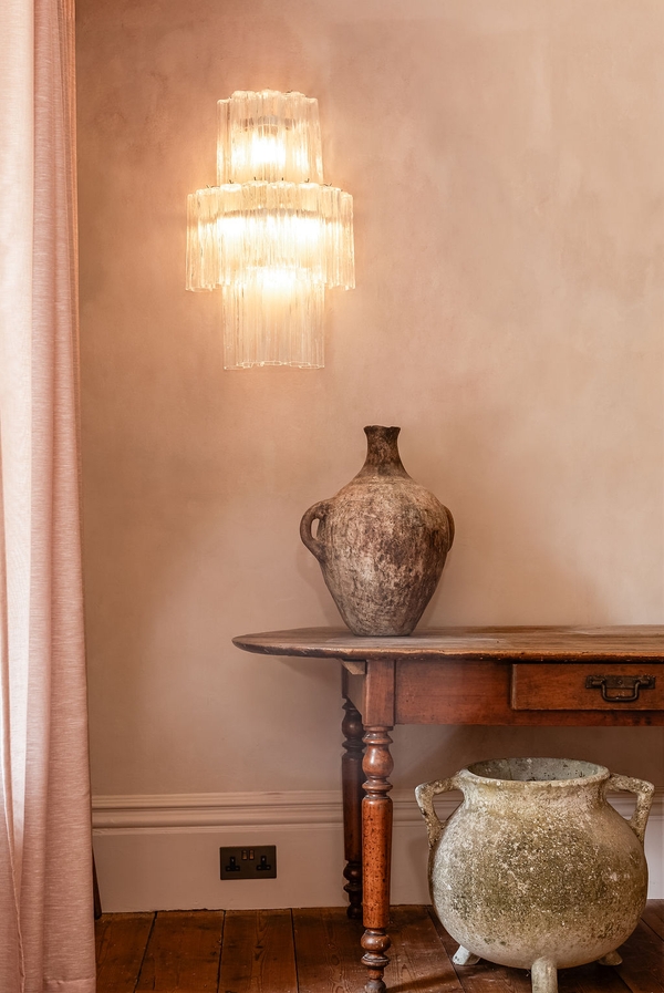 Classical wooden console table styled beneath a crystal chandelier on a pale pink plaster backdrop wall from Love Locations.