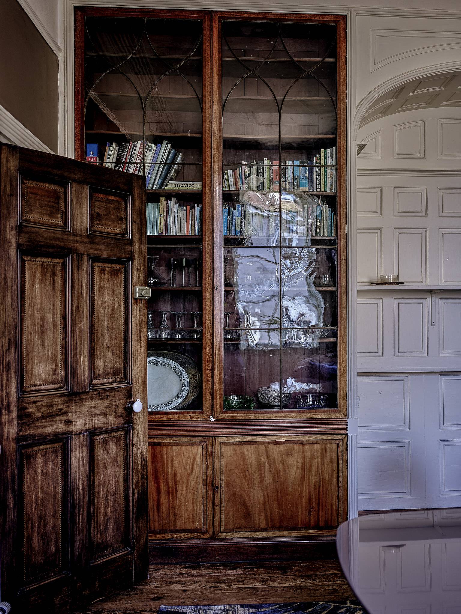 Historic dark wood display cabinet set beside white wood-panelled walls in a Kent location home, Love Locations.