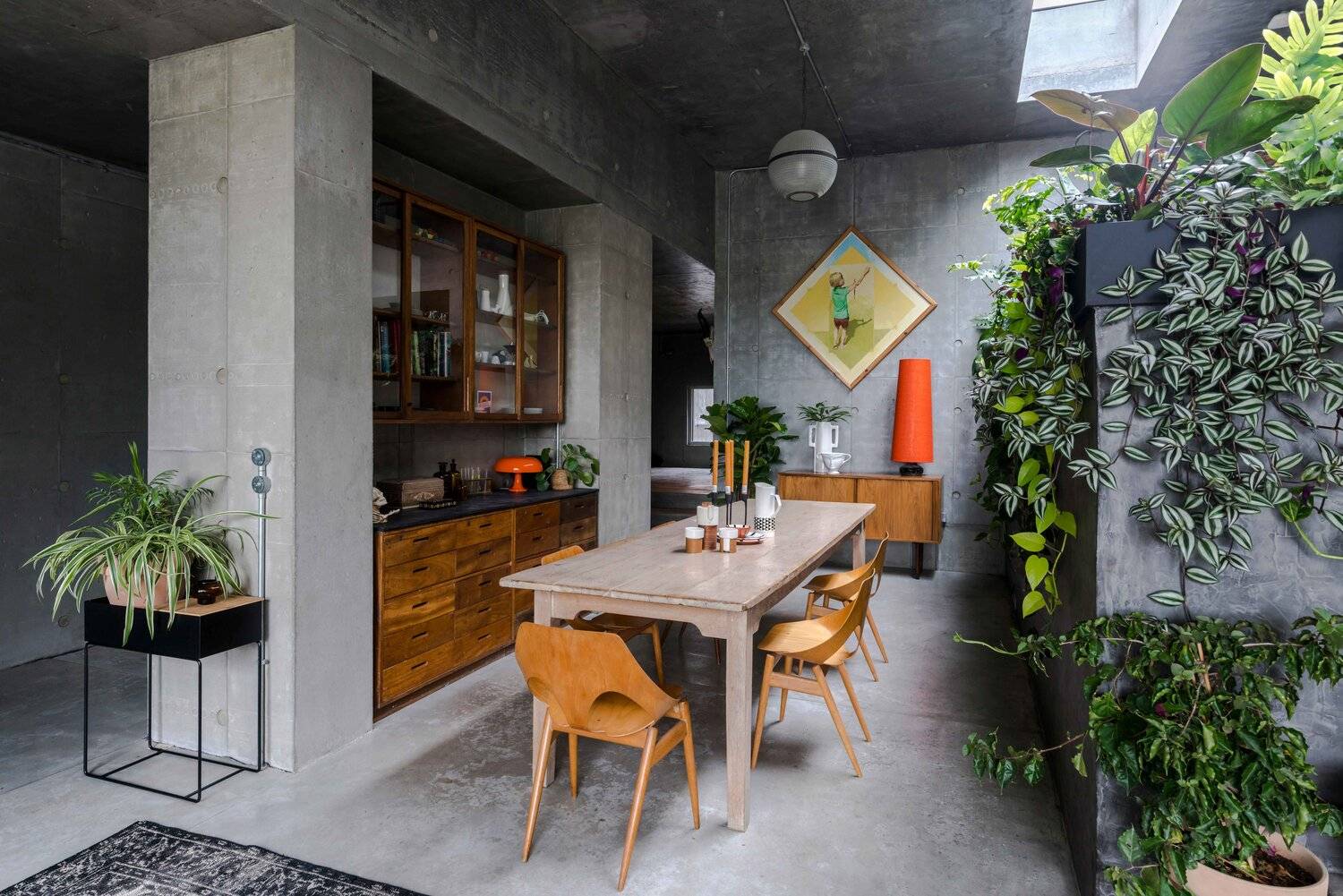 Brutalist board-marked concrete dining room shoot location in Plumpton Green, BN7 featuring a rustic timber dining table, orange chairs, and internal living plant wall via Love Locations.