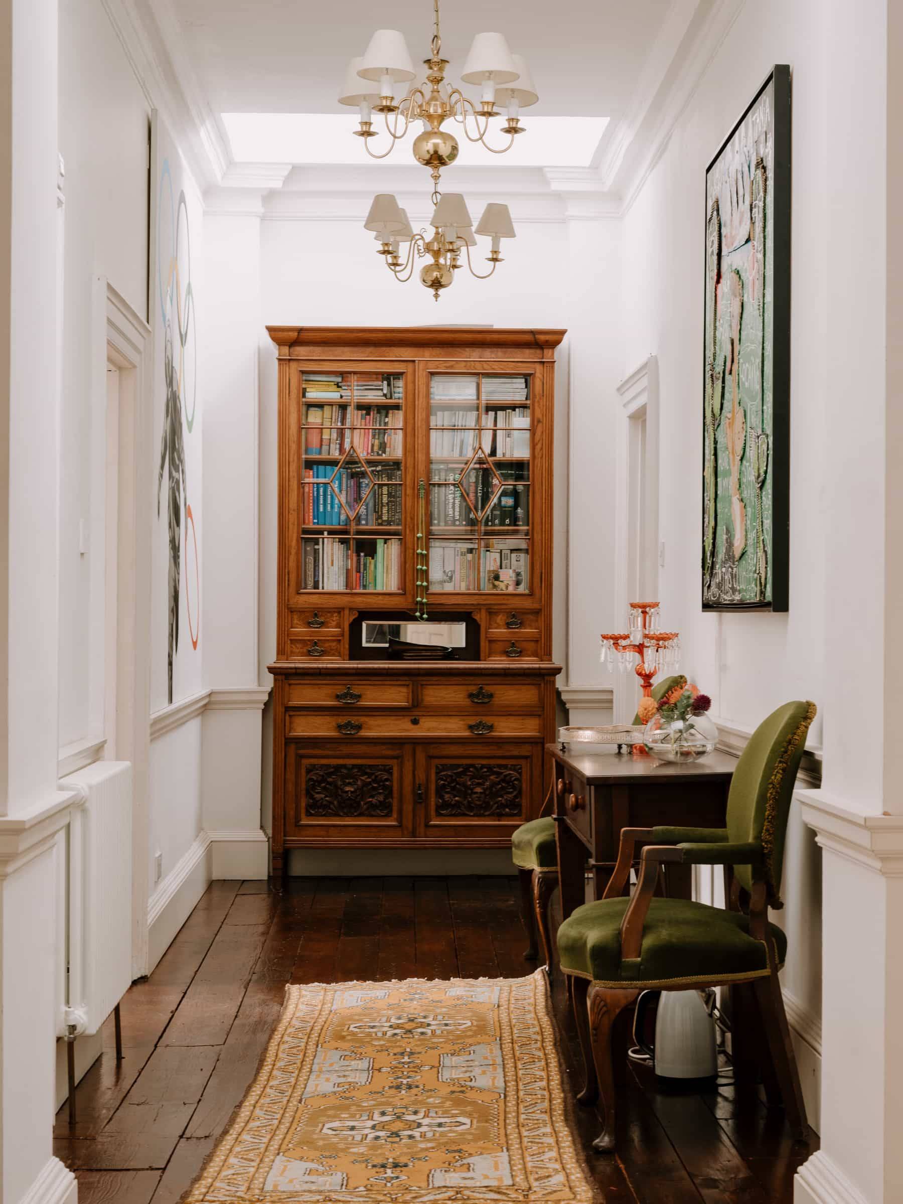 Corridor hallway transition featuring an antique dark wood glass display cabinet and green velvet armchair, Love Locations RG42.