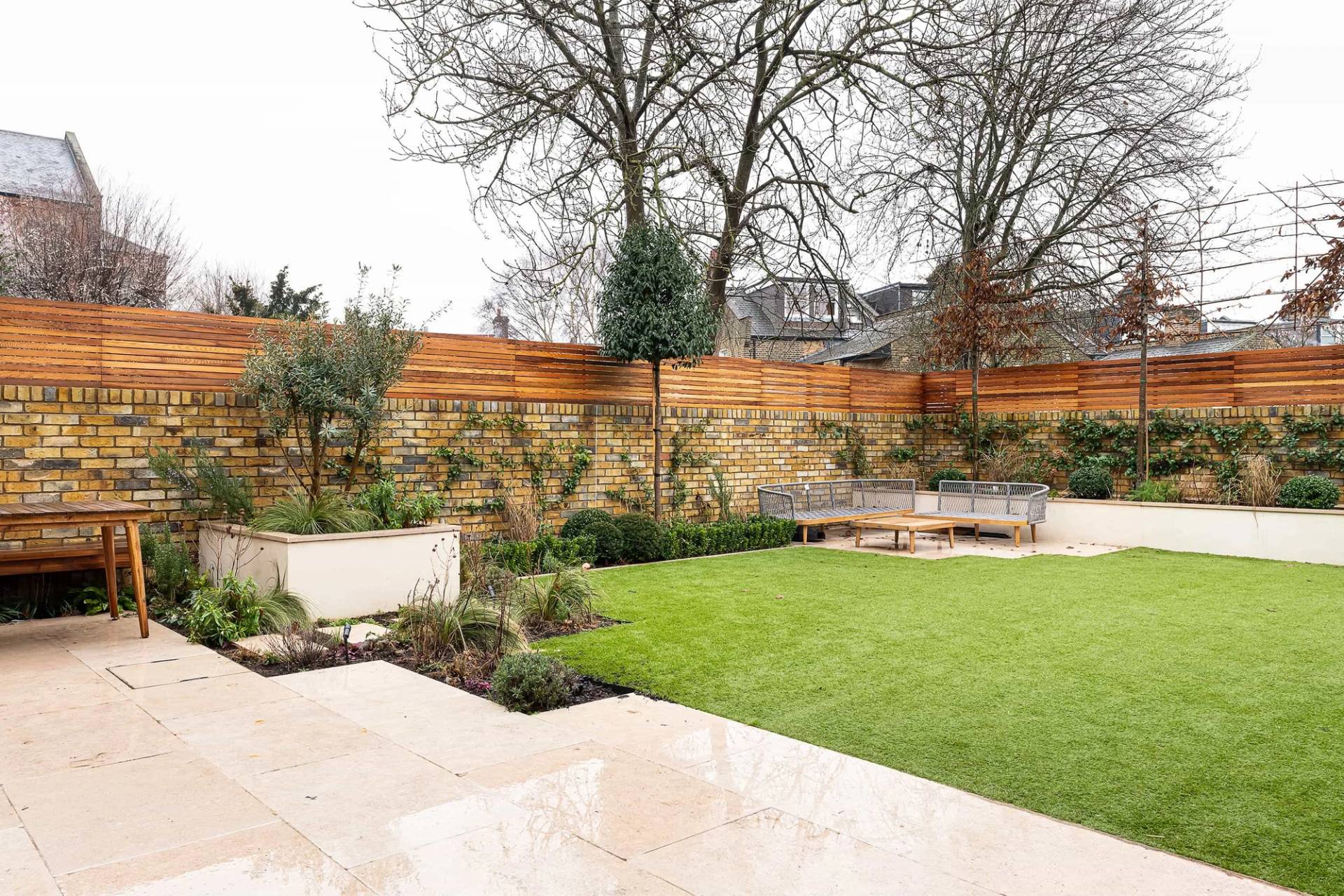 Manicured green lawn garden with raised stone planter beds and a wooden garden bench in Queens Park, Love Locations.