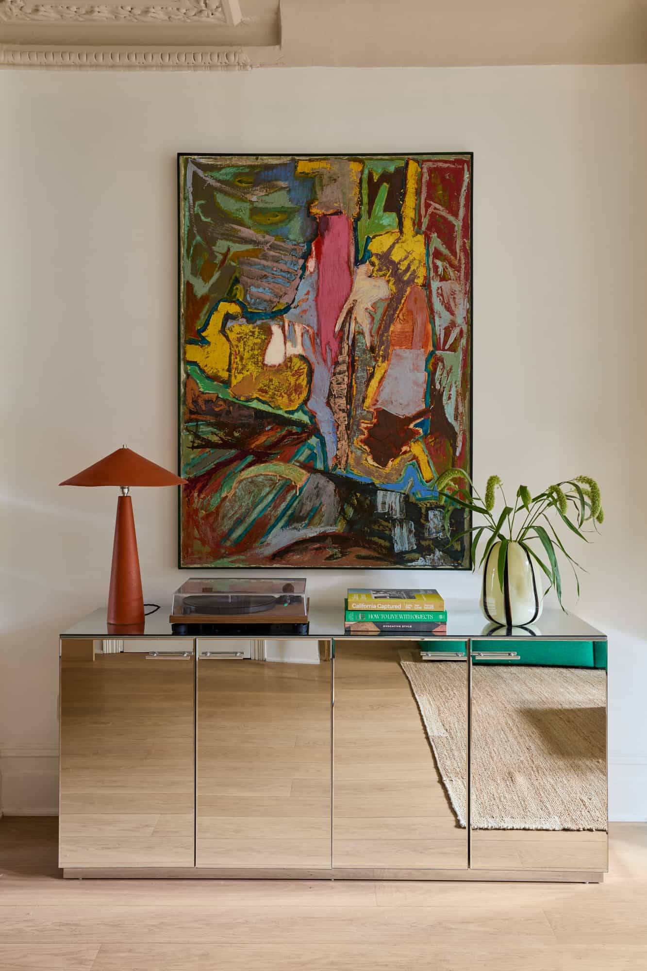 Love Locations mid-century modern shoot space Lewisham: Glamorous mirrored sideboard cabinet displaying a large colorful abstract painting and statement table lamp, perfect for lookbooks.