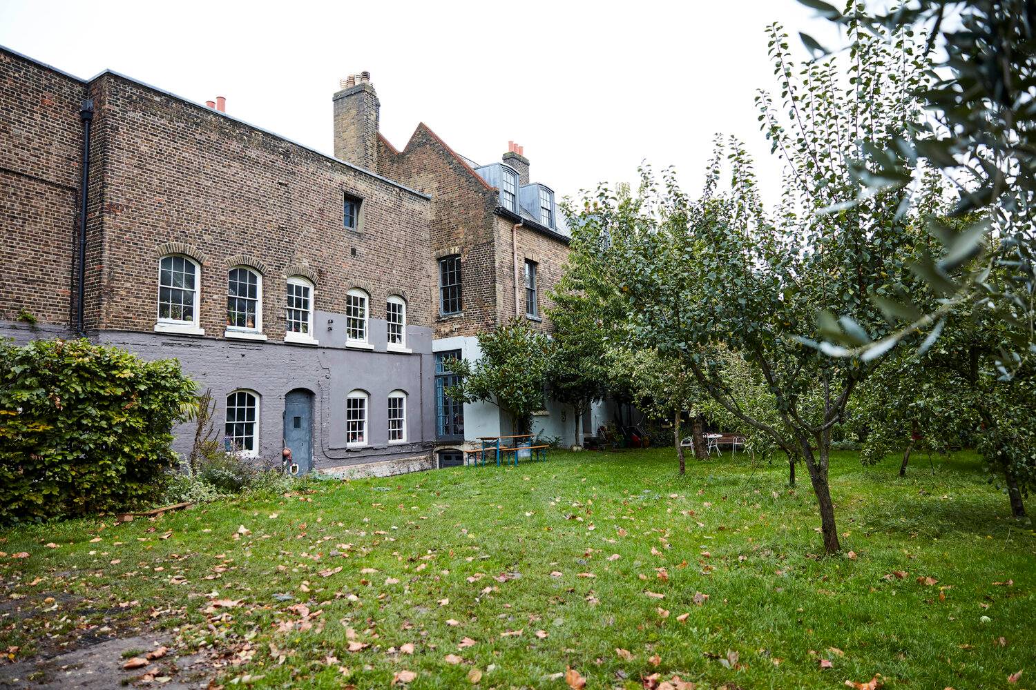 Rear garden elevation of a historic brick house with orchard trees and expansive lawn grounds, ideal for outdoor lifestyle shoots, Love Locations SE8.