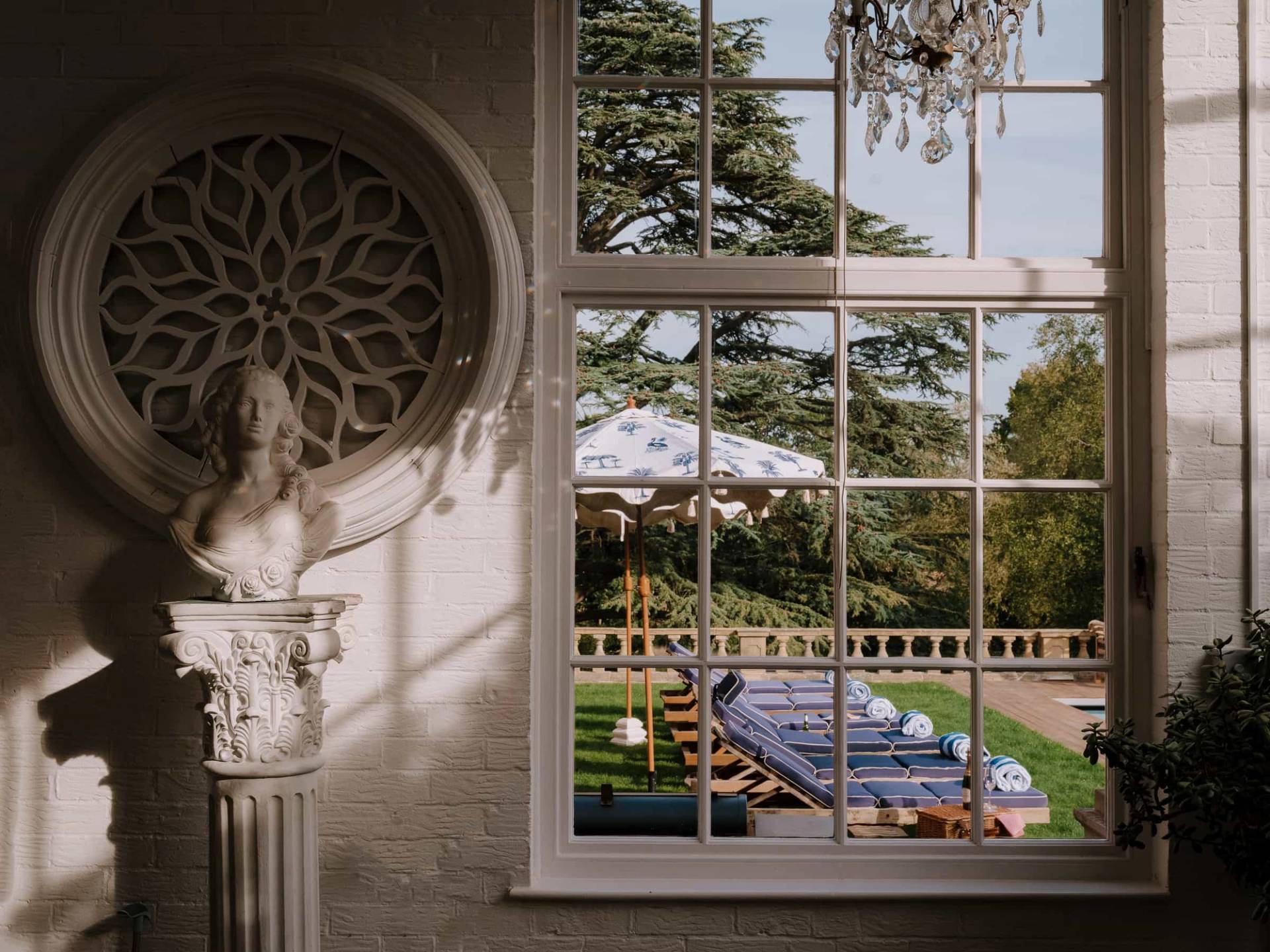 View through an arched sash window looking out towards a sunny outdoor swimming pool and sun loungers, Love Locations RG42.