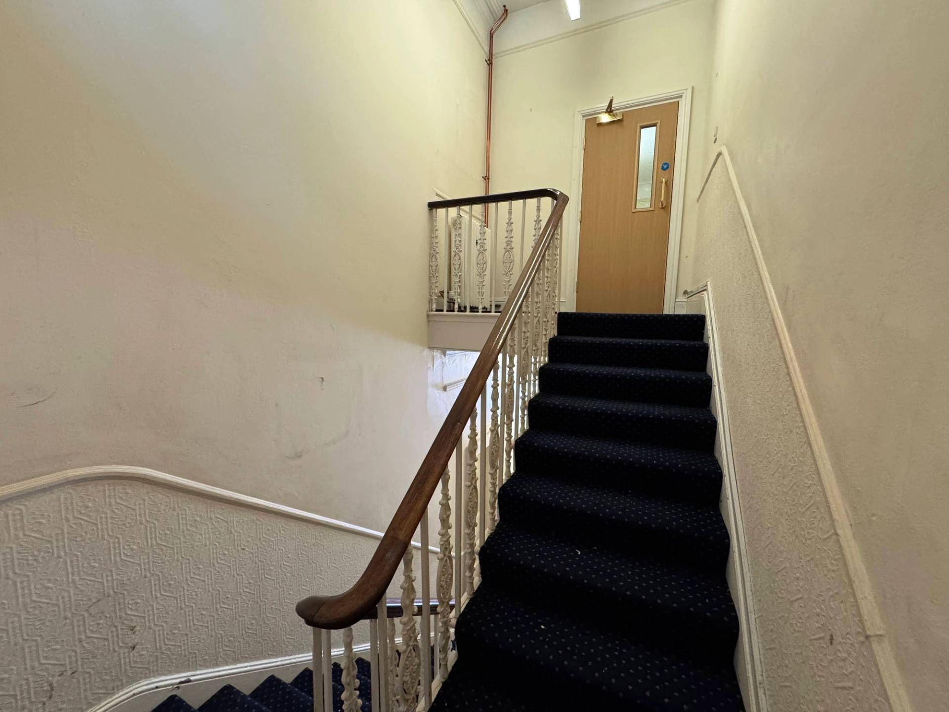 Grand period staircase featuring a dark carpet, white balustrades, and a polished wooden handrail, managed by Love Locations.