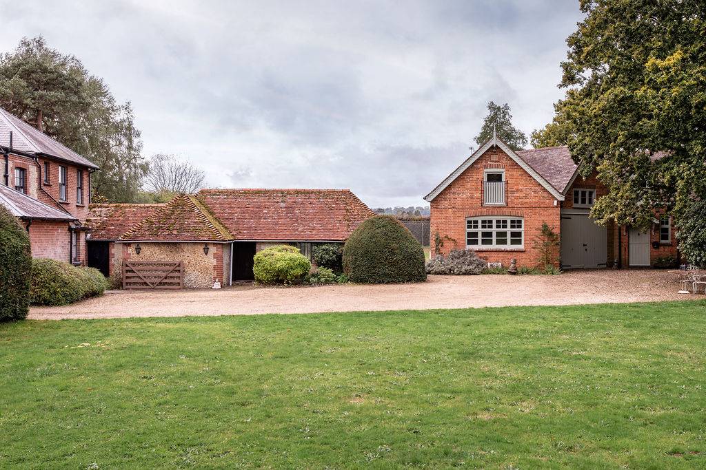 Expansive lawn with traditional brick outbuildings and gravel courtyard at a character property in Liss, Hampshire GU33, represented by Love Locations.