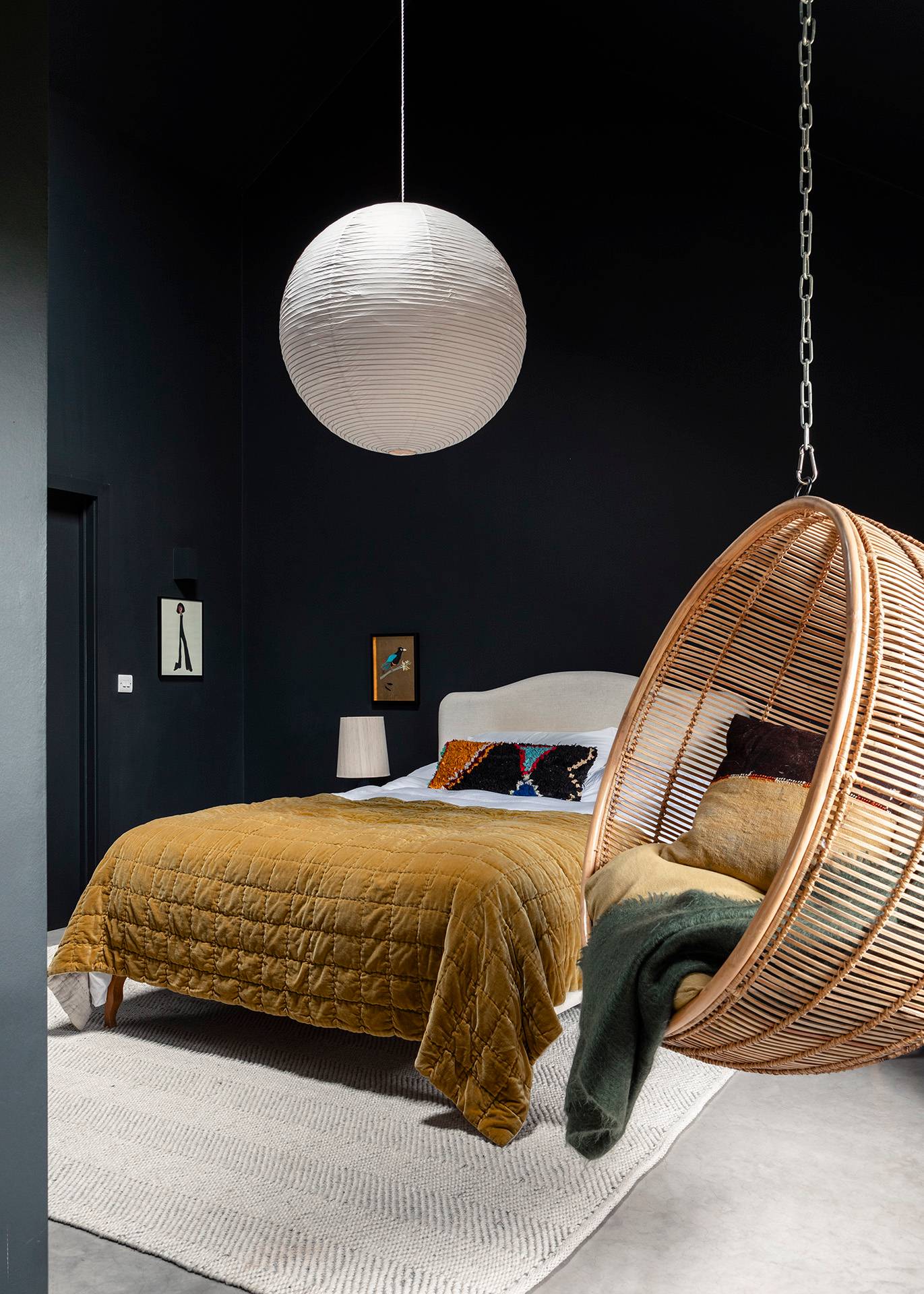 Moody dark navy bedroom suite featuring a mustard throw, white paper globe light, and hanging rattan swing chair, Love Locations SN8.