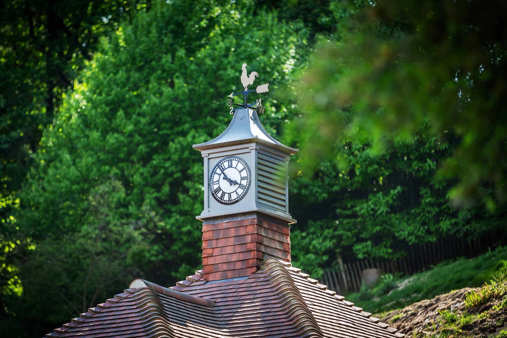 Detailed architectural view of a historic clock tower and weather vane set above timber roofs, ideal for period film backdrops, Love Locations GU27.