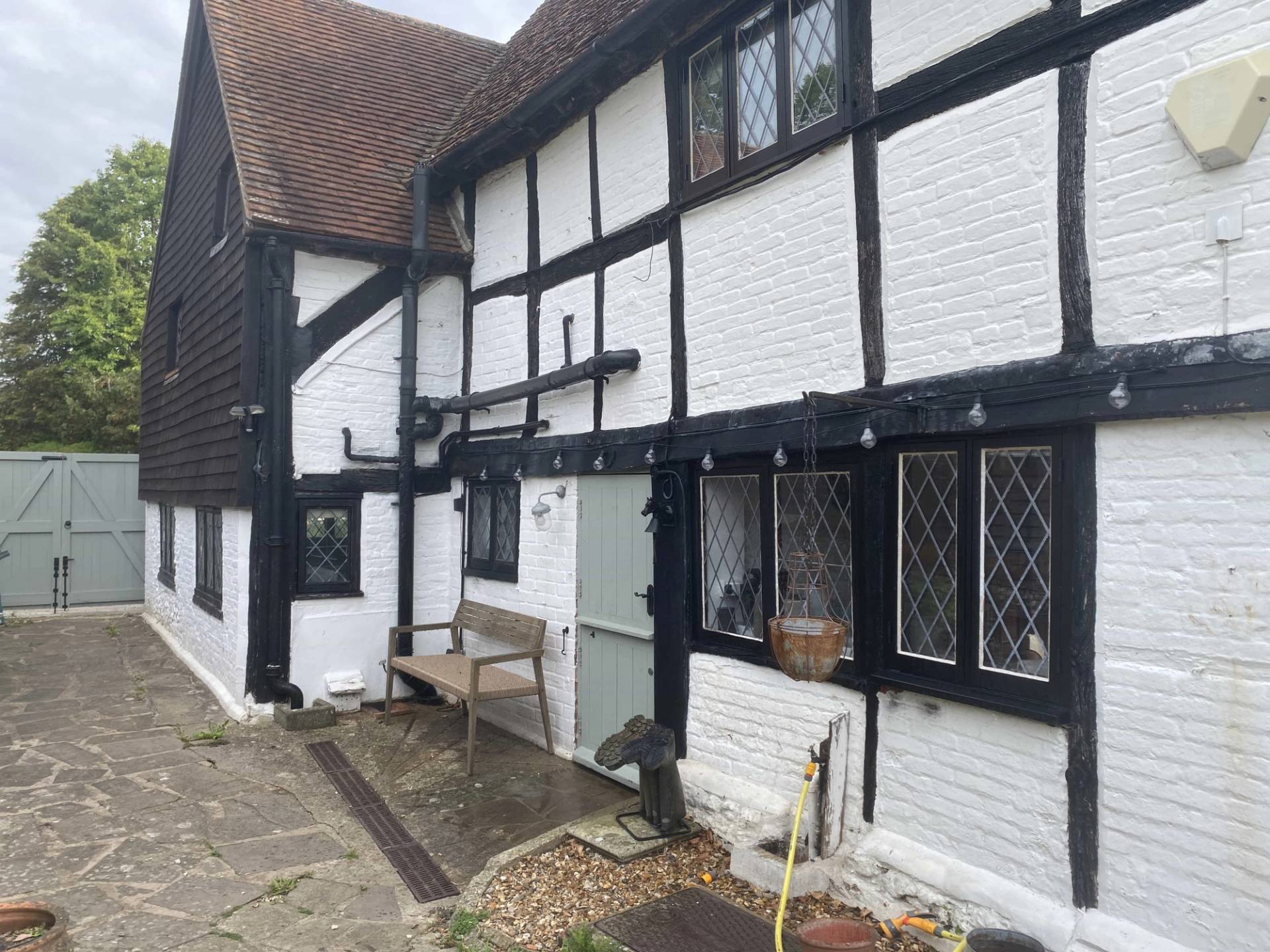 Rear exterior view of a historic Tudor cottage featuring traditional black-and-white timber framing, outdoor bench seating, and stone paving, Love Locations RG9.