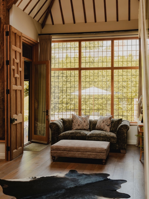 Light-filled barn lounge corner with a grey ottoman coffee table set before floor-to-ceiling multi-pane windows, perfect for interior lookbooks, Love Locations RG9.