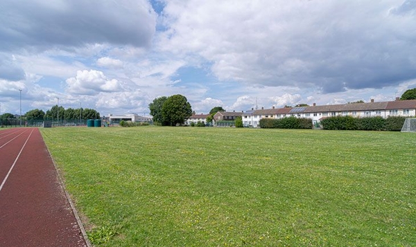 Love Locations expansive school field shoot space SE2: Sprawling natural grass playing field bordered by mature trees and residential backgrounds, great for outdoor school yard tracking shots.