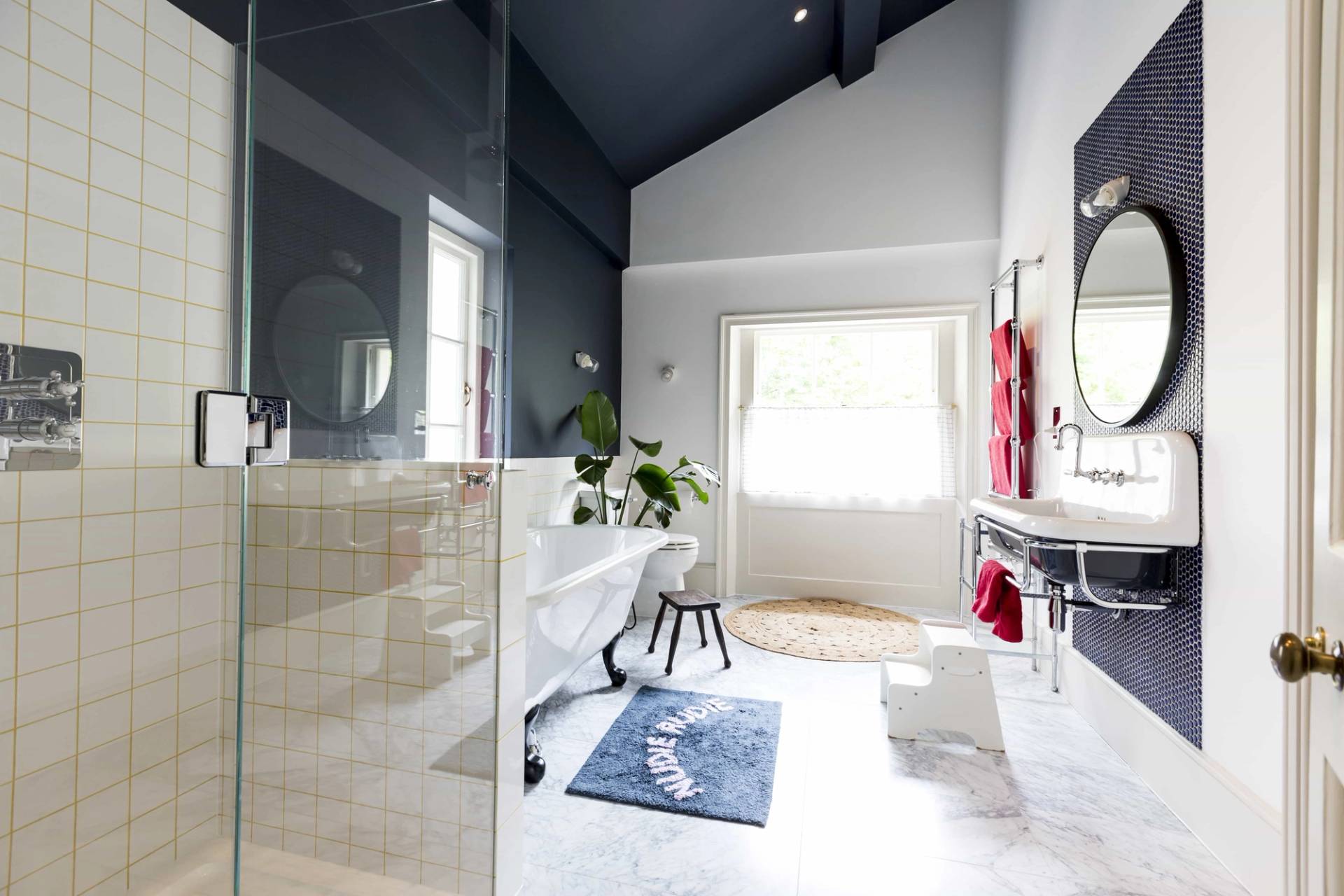 Light-filled loft bathroom in Camberwell, SE5 with navy blue ceiling, white tub, and marble flooring via Love Locations.