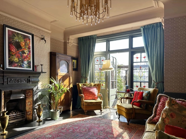 Sunlit living room with French doors opening onto a green garden, period fireplace, and velvet armchairs, Love Locations N13.