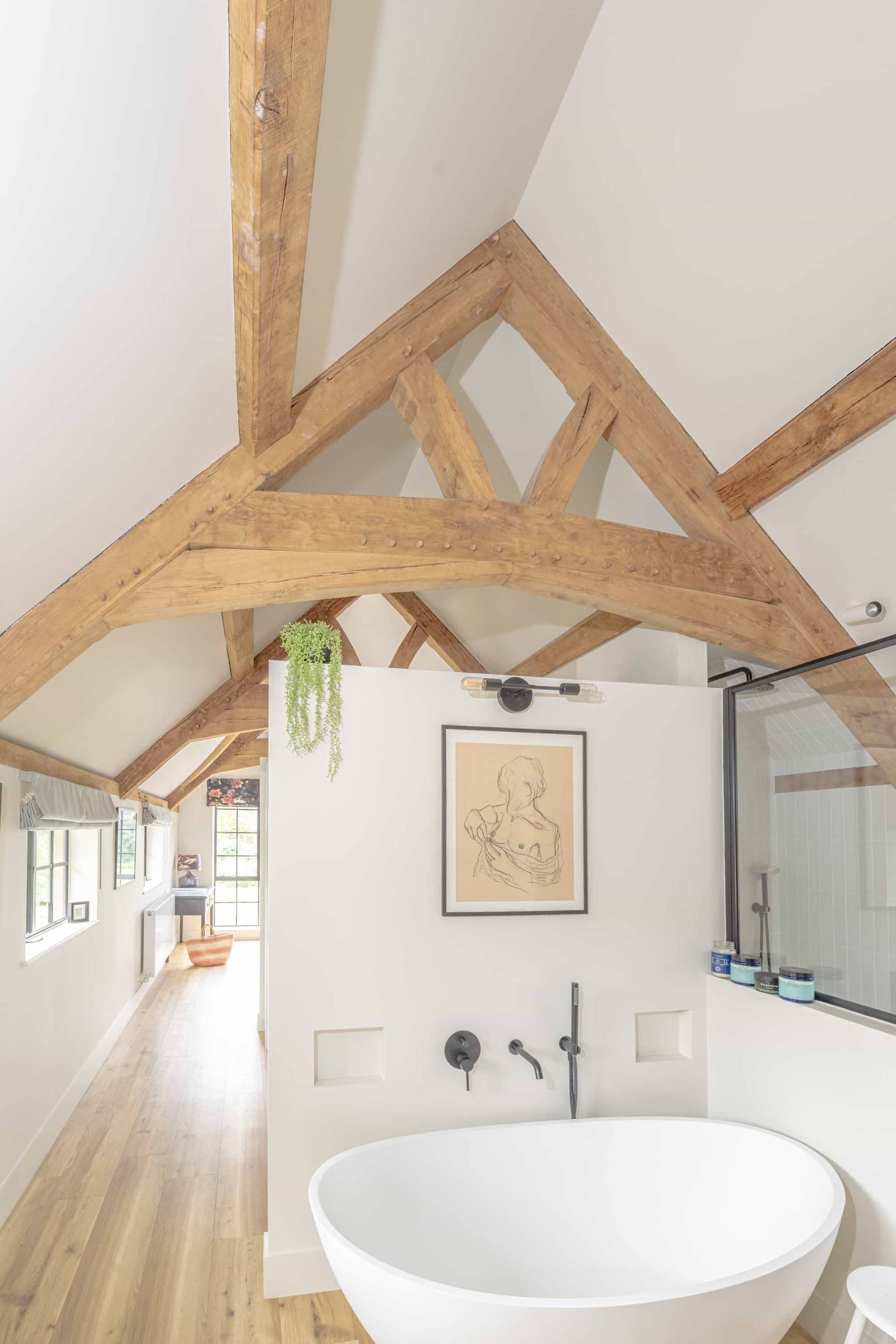 Ensuite bathroom set under vaulted oak roof beams featuring a walk-in glass shower enclosure, Love Locations GU28.