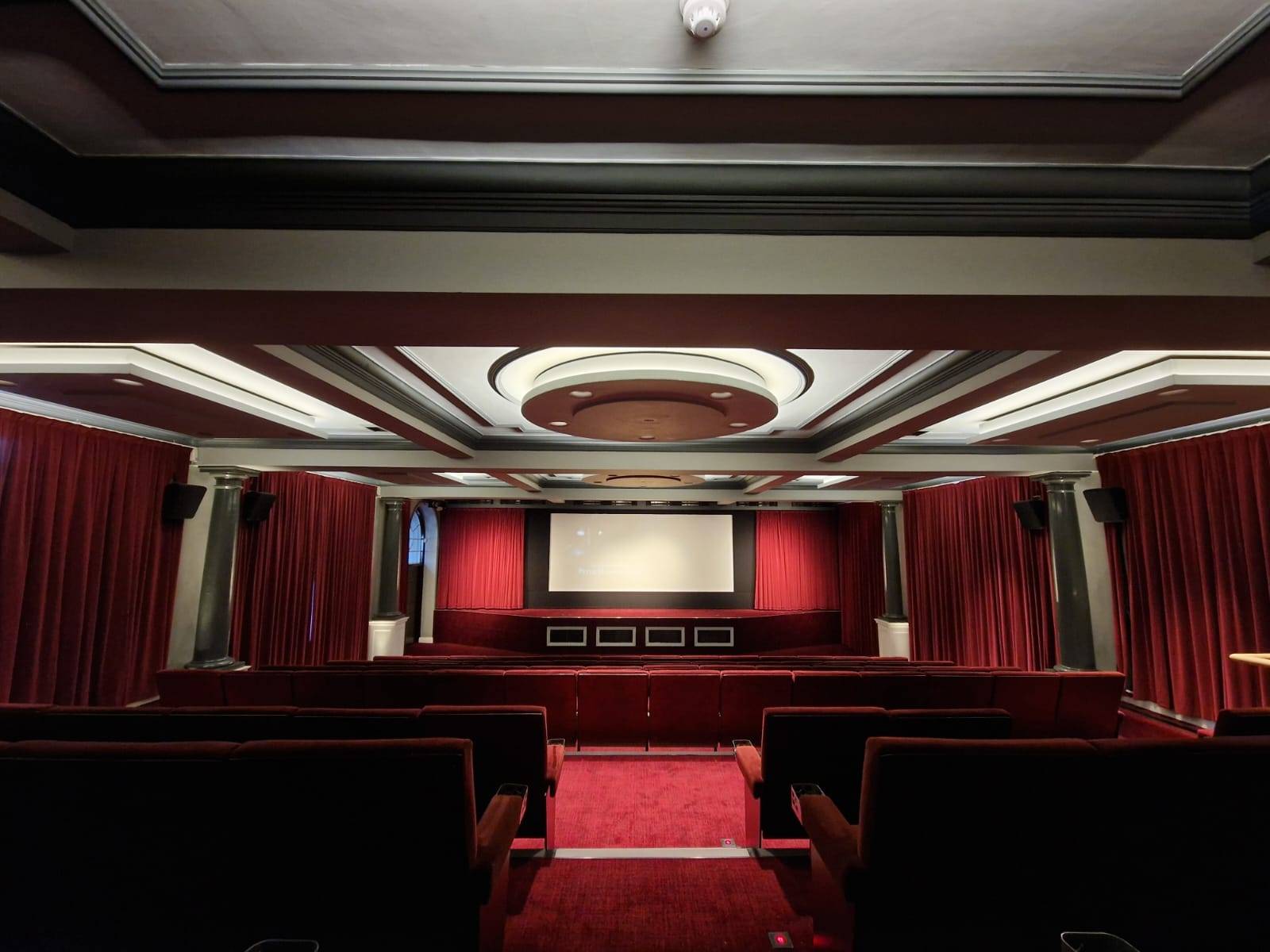 Intimate vintage cinema room film location in Lewisham SE6 via Love Locations, featuring dark red plush seats, a screening projection screen, and patterned ceiling panels.