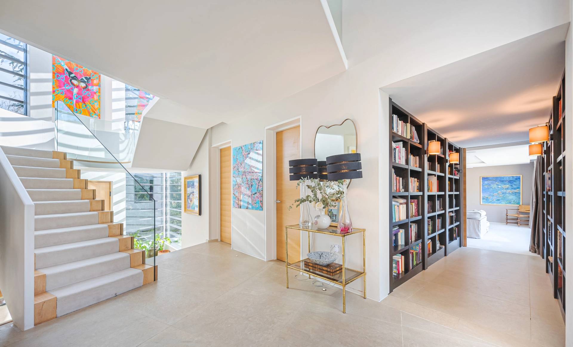 Double-height entrance hallway featuring a floating glass balustrade staircase and bookshelf alcoves, Love Locations KT2.